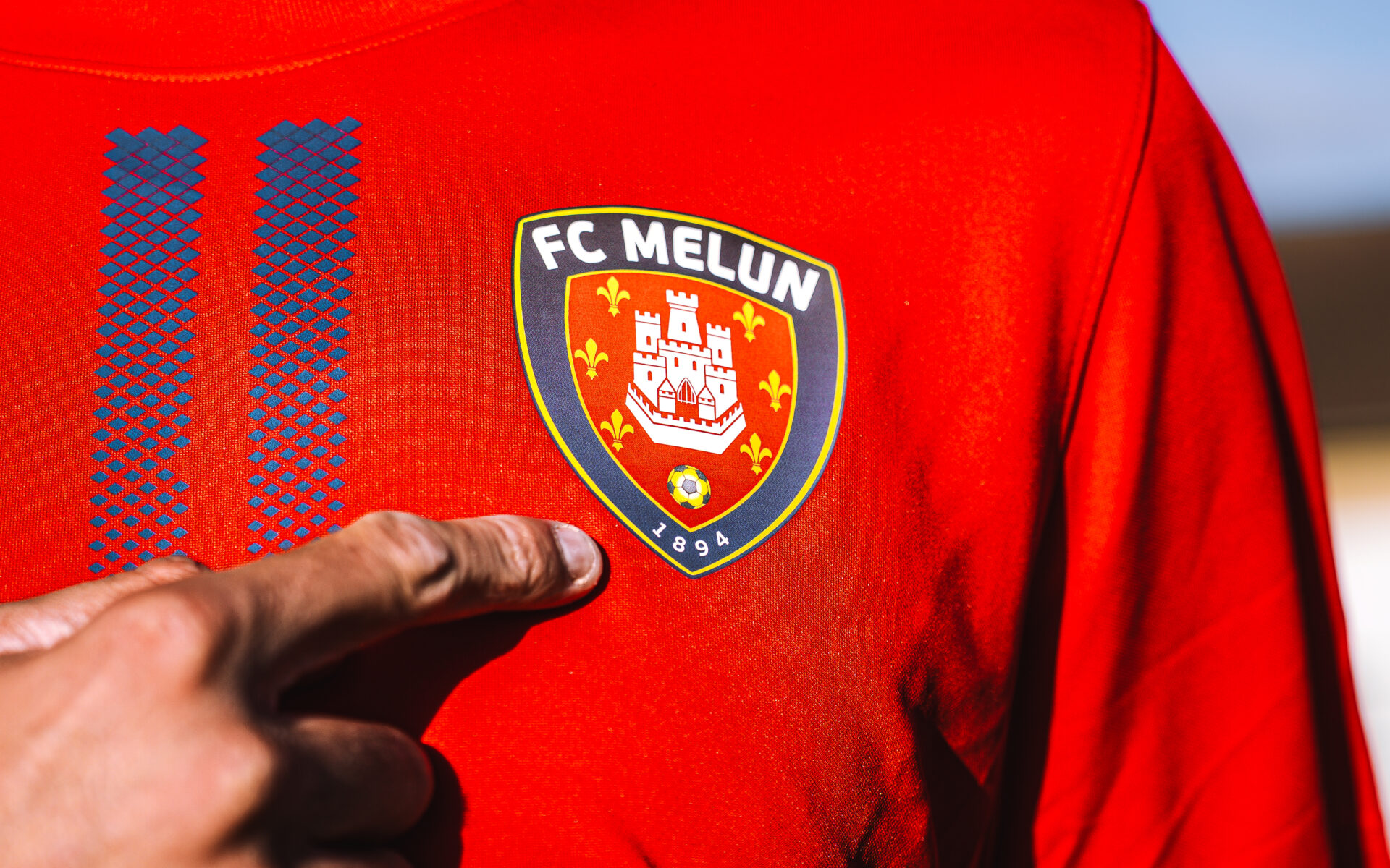 Joueur du FC Melun désignant le blason du club, fondé en 1894, sur son maillot rouge